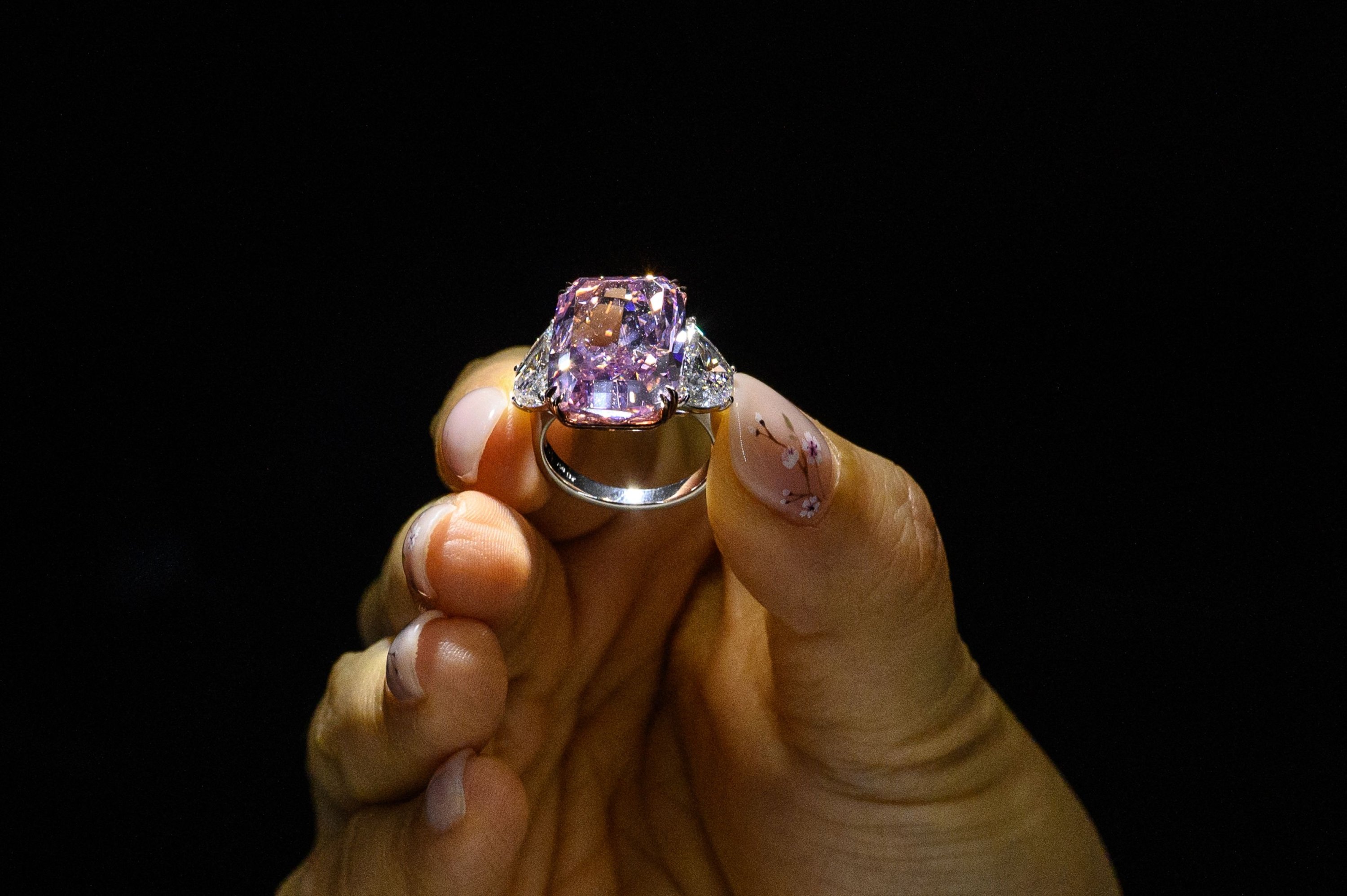 A woman displays the Sakura Diamond, a 15.81 carat fancy vivid purple-pink diamond ring, during a Christies pre-auction preview in Hong Kong, May 20, 2021. (AFP Photo)