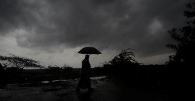 A villager walks holding an umbrella as dark clouds loom overhead in Balasore district in Odisha, India, Tuesday, May 25, 2021. (AP Photo)