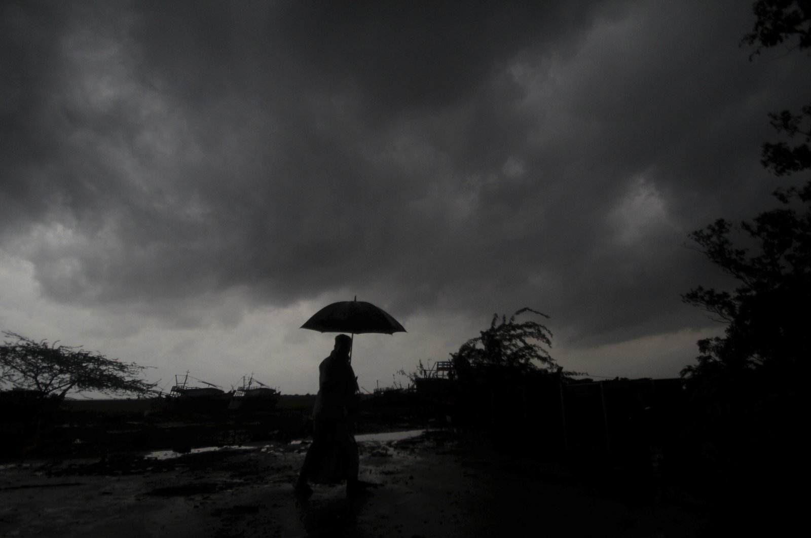 A villager walks holding an umbrella as dark clouds loom overhead in Balasore district in Odisha, India, Tuesday, May 25, 2021. (AP Photo)