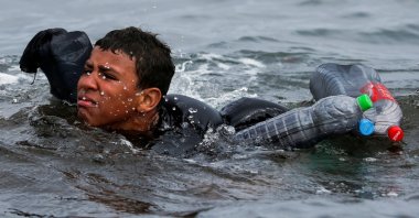 A Moroccan boy swims using bottles as a float, near the fence between the Spanish-Moroccan border, after thousands of migrants swam across the border, in Ceuta, Spain, May 19, 2021. (Reuters Photo)
