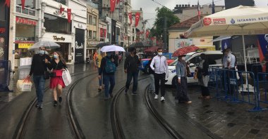 People wearing masks walk amid rainy weather at the entrance of Istiklal Avenue at the famous Taksim Square in Istanbul, Turkey, May 29, 2021. (IHA Photo)