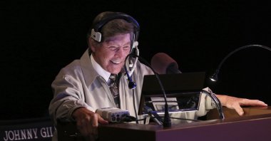 In this image provided by Jeopardy Productions, Inc., show announcer Johnny Gilbert appears on the set of "Jeopardy!" Gilbert worked with host Alex Trebek for 37 years and was reluctant to continue after losing his admired colleague. But others with the show urged him to consider his role as a comforting touchstone for viewers who also were in mourning. (Carol Kaelson/Jeopardy Productions, Inc. via AP)