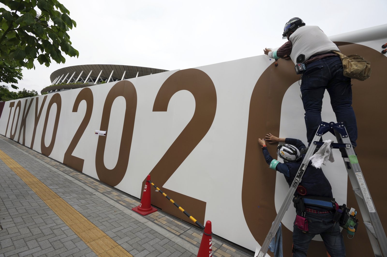 Workers paste the overlay on the wall of the National Stadium, where the opening ceremony and many other events are scheduled for the Tokyo 2020 Olympics, Tokyo, Japan, June 2, 2021. (AP Photo)