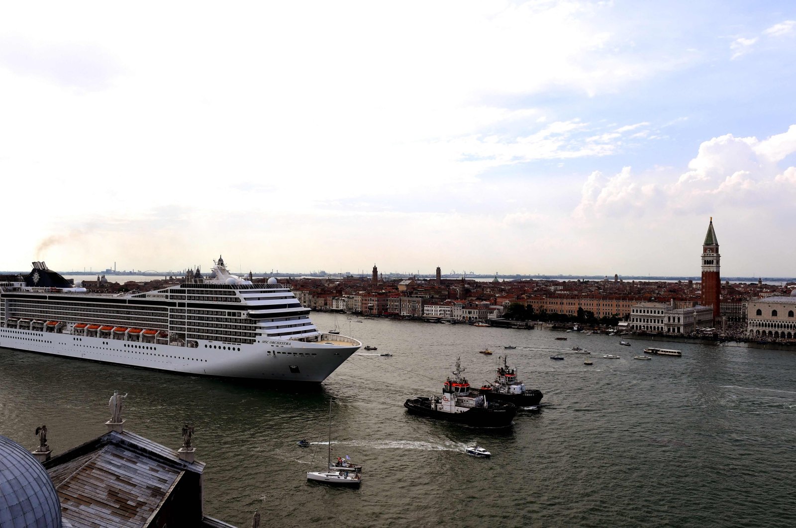 Tugboats escort the MSC Orchestra cruise ship across the basin past the Bell Tower and the Doge's Palace as it leaves Venice, Italy, June 5, 2021. (AFP Photo)