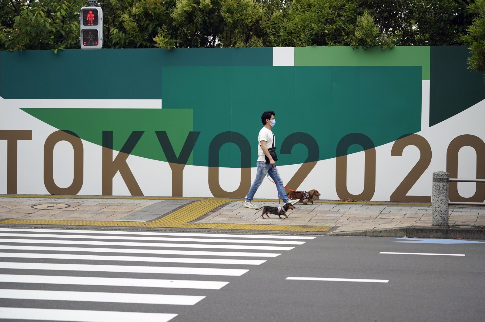 A man strolls with his pet dogs past a Tokyo Olympics advertising board in Tokyo, Japan, June 3, 2021. (EPA Photo)