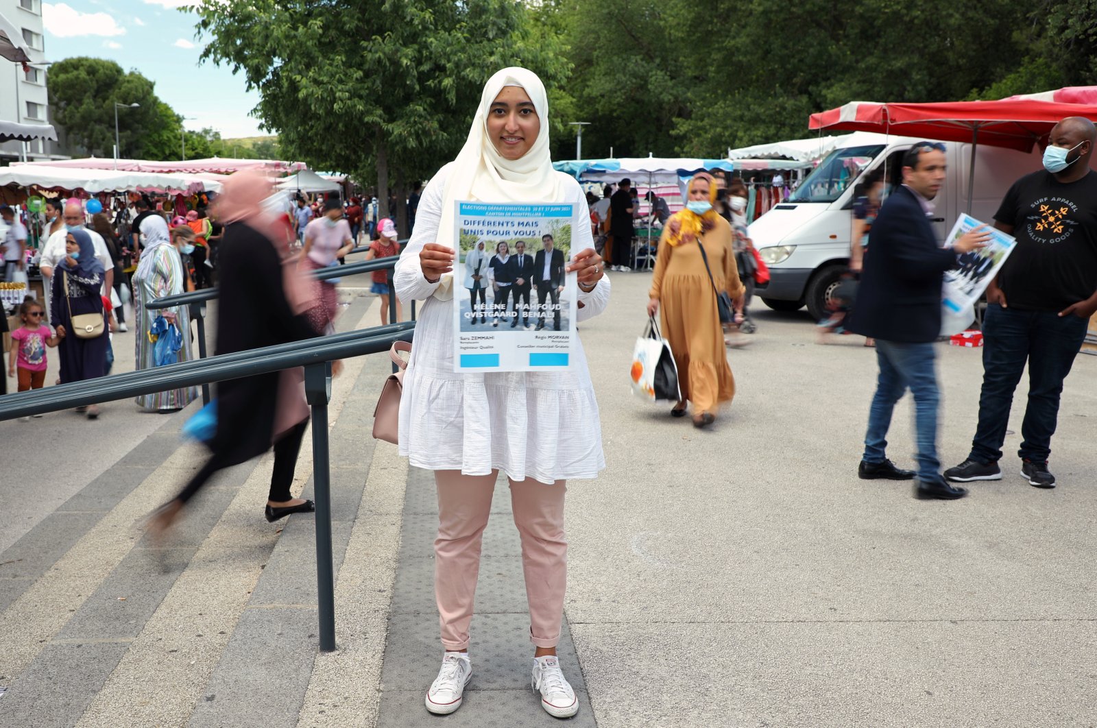 French local election candidate Sara Zemmahi, wearing a headscarf, holds her campaign flyer with the slogan "Different, but united for you" as she poses during an interview for Reuters ahead of the upcoming French local elections in the La Mosson market in Montpellier, France, June 5, 2021. (Reuters Photo)