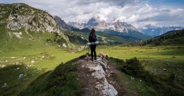 A young hiker with a backpack walks on a mountain trail with a dog. (Shutterstock Photo)