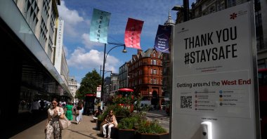 Pedestrians, some wearing face coverings due to COVID-19, walk past a coronavirus information sign as they pass shops on Oxford Street in central London on June 7, 2021. (AFP Photo)