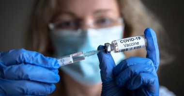 COVID-19 vaccine in researcher's hands. (Shutterstock Photo) 