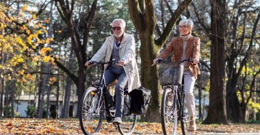 A mature fit couple ride bicycles in a public park. (Shutterstock Photo)