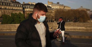A man walks with a face mask to prevent the spread of the COVID-19 coronavirus, as a man takes a snapshot of the sunset, in Paris, March 29, 2021. (AP Photo)
