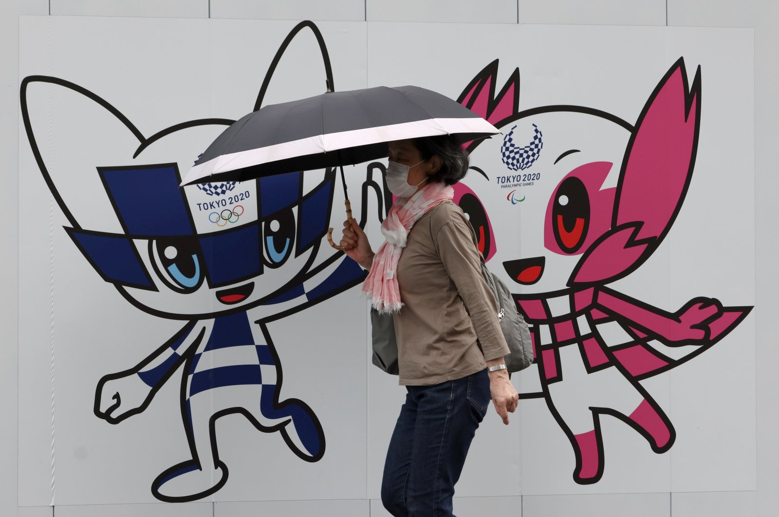 A woman wearing a protective face mask against the coronavirus walks in front of a wall decoration featuring Tokyo 2020 Olympic Games mascot Miraitowa and Paralympics mascot Someity, Tokyo, Japan, May 28, 2021. (Reuters Photo)