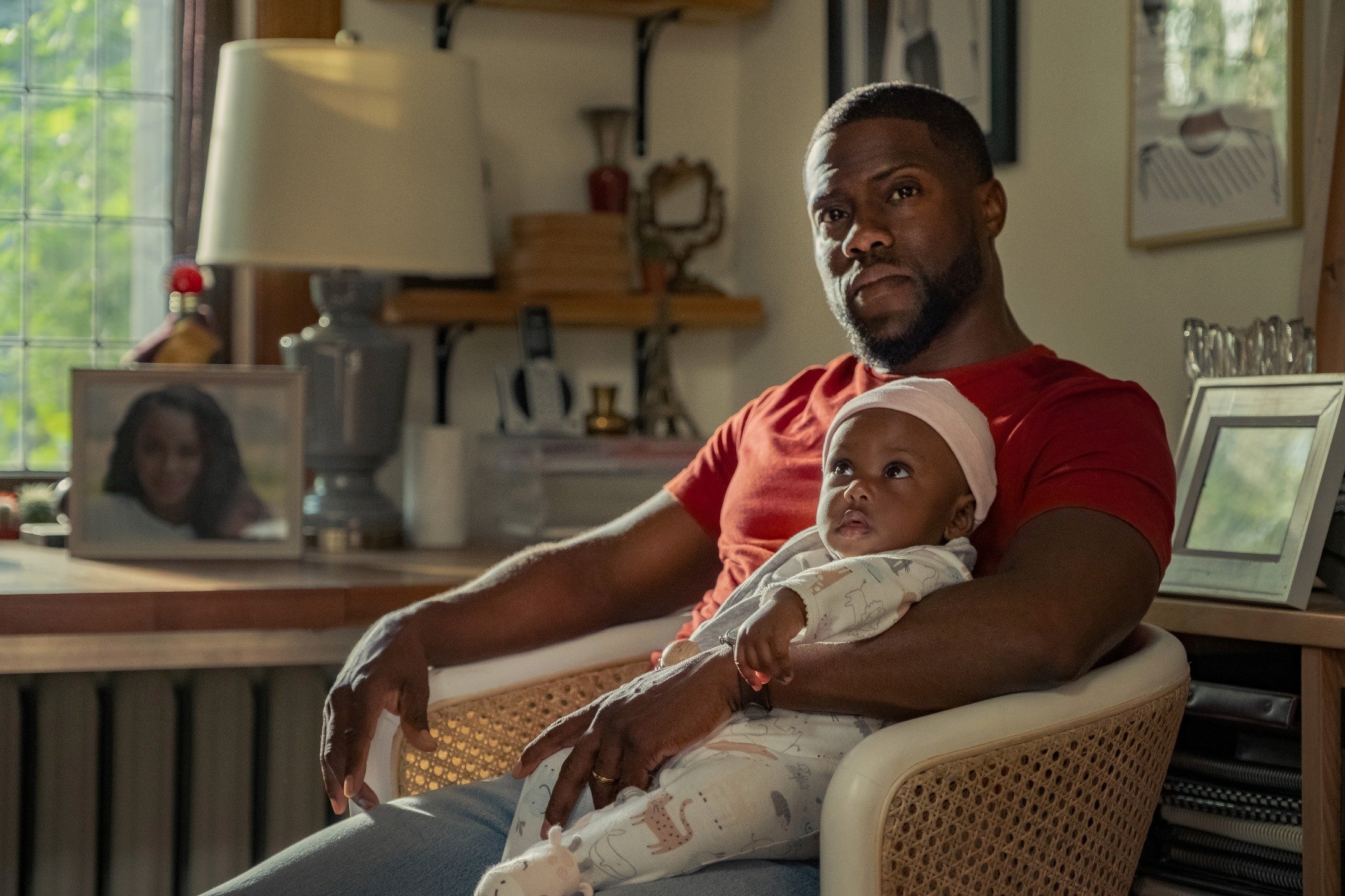 Kevin Hart hold a baby on his lap in a scene from the movie "Fatherhood." (Netflix via AP)