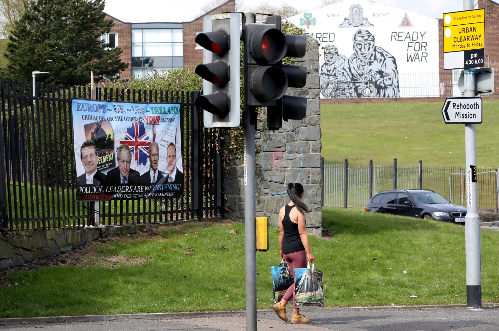 A woman walks past a pro-Loyalist, anti-Northern Ireland Protocol poster (L) in Belfast, Northern Ireland on April 19, 2021. (AFP Photo)