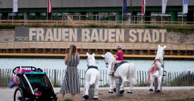 Children play in a playground facing large panels proclaiming the slogan "Women build the city" next to some of the building sites that will eventually contain 12,000 new housing units, at Vienna's suburb Seestadt, Austria, June 8, 2021. (AFP Photo)