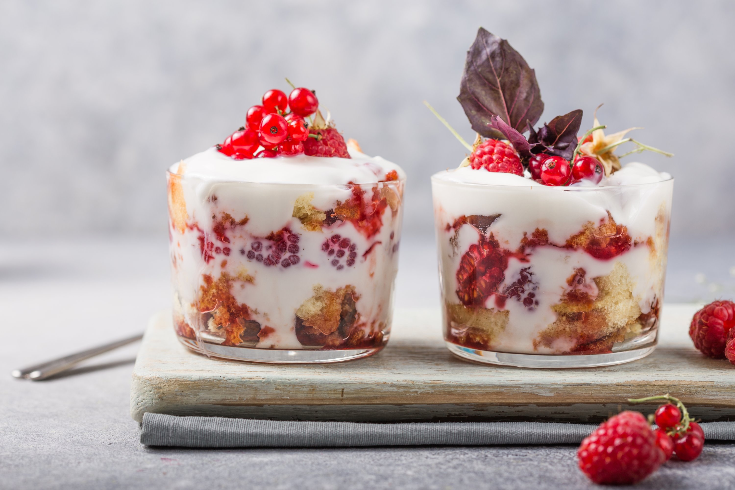 Layered trifle dessert with sponge cake, whipped cream and raspberries in serving glasses on a light background. (Shutterstock Photo)