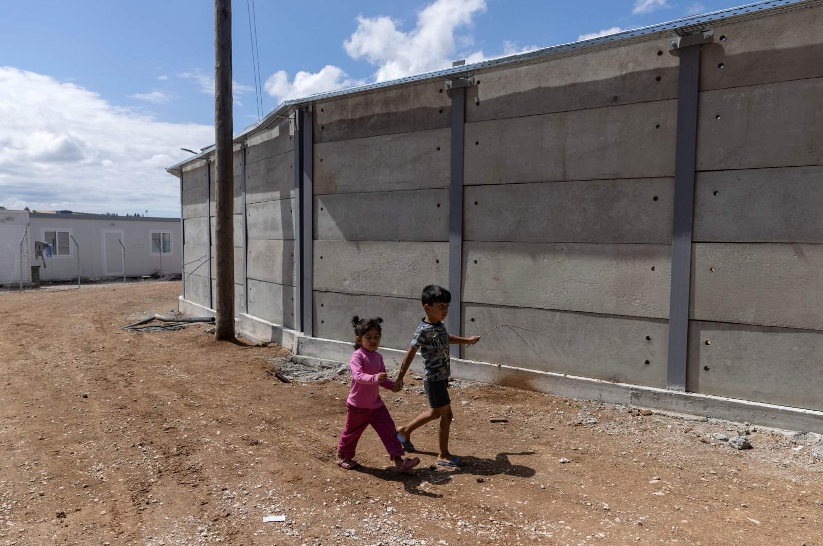 Children walk next to a newly built concrete wall inside the Ritsona camp for refugees and migrants, in Greece, June 15, 2021. (Reuters Photo)