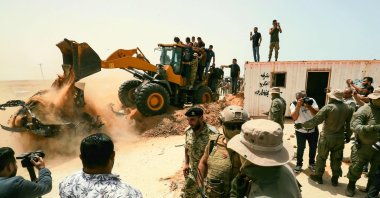 People cheer as an excavator removes rubble during a ceremony marking the reopening of a road between the cities of Misrata and Sirte, in the town of Buwairat al-Hassoun, Libya, June 20, 2021. (AFP Photo)