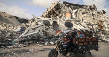 A Palestinian man transports children in a tricycle past the Al-Shuruq building, destroyed by an Israeli airstrike, after a cease-fire was agreed upon between Israel and Hamas, in Gaza City, Palestine, May 21, 2021. (AFP Photo)