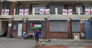 A boy kicks a football in front of the balconies and landings adorned with predominantly England flags at the Kirby housing estate in London, England, June 29, 2021. (AP Photo)