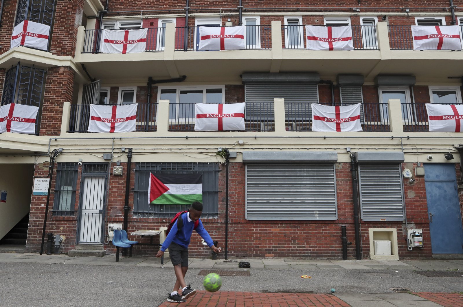A boy kicks a football in front of the balconies and landings adorned with predominantly England flags at the Kirby housing estate in London, England, June 29, 2021. (AP Photo)