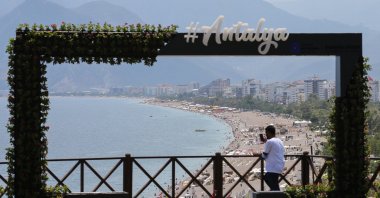 A sign that says "#Antalya" can be seen against a backdrop of a sandy beach and mountain ranges in Antalya, Turkey, June 28, 2021. (AA Photo)