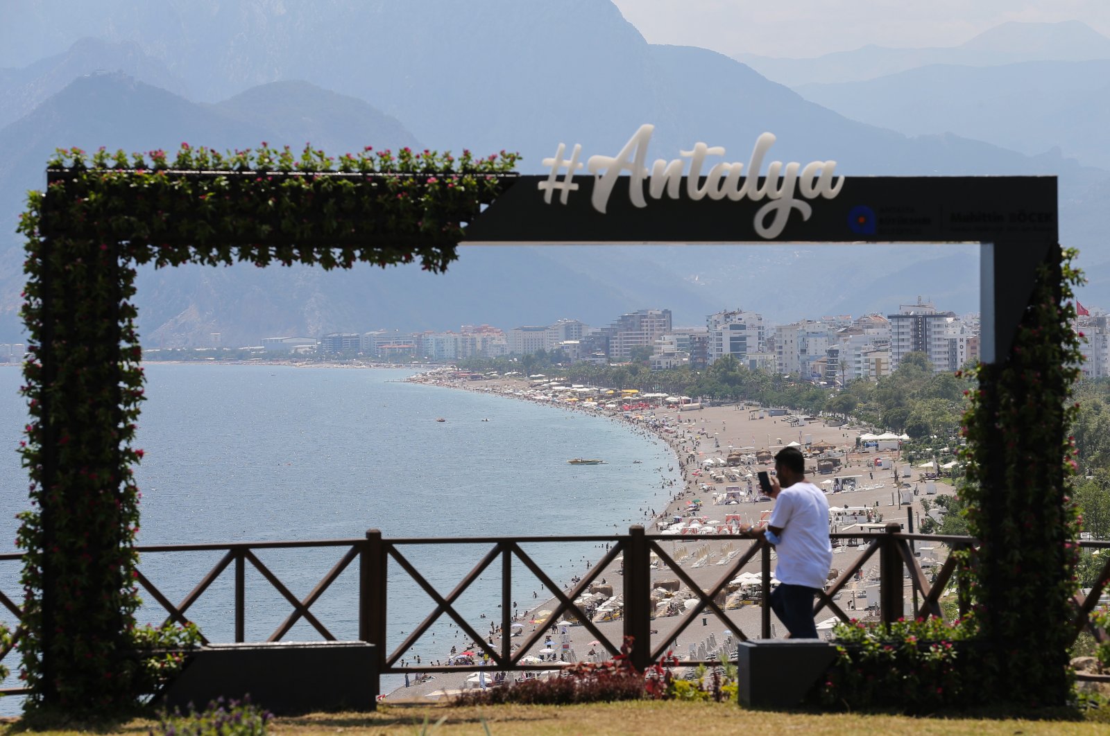 A sign that says "#Antalya" can be seen against a backdrop of a sandy beach and mountain ranges in Antalya, Turkey, June 28, 2021. (AA Photo)