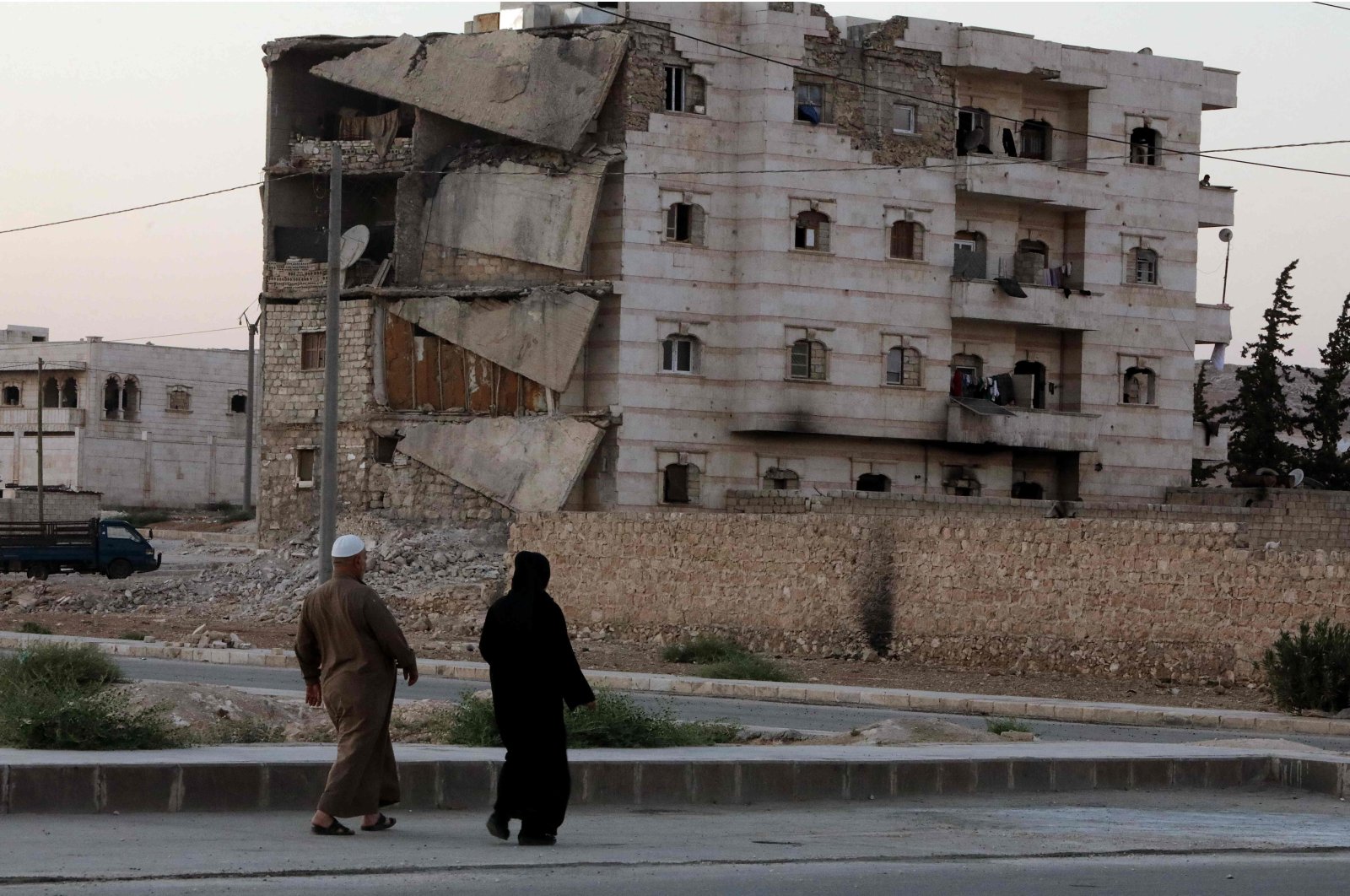 Syrians walk past a damaged building in the opposition-held city of al-Bab northwest of Aleppo in northern Syria, on June 23, 2021. (AFP Photo)