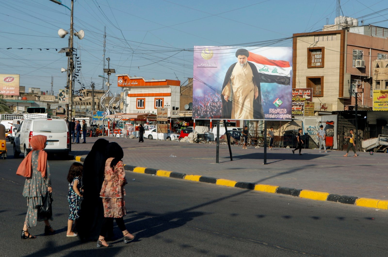 Iraqi women cross a street near a poster of Iraqi Shiite cleric Muqtada al-Sadr in the Sadr City district of Baghdad, Iraq, June 21, 2021. (Reuters File Photo)