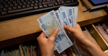 A currency exchange office worker counts Turkish Lira banknotes in front of the electronic panel displaying currency exchange rates at an exchange office in Istanbul, Turkey, Aug. 6, 2020. (AFP Photo)