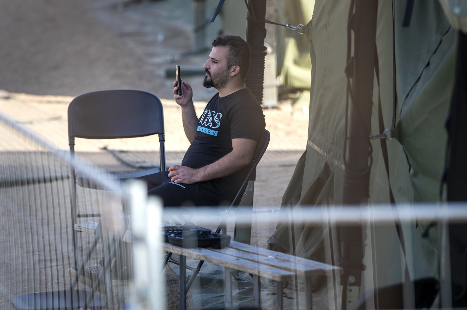 A migrant uses a mobile phone as he sits outside a tent at the newly built refugee camp in the town of Pabrade, some 40 kilometers (24.8 miles) northeast from Vilnius, Lithuania, July 3, 2021.  (AP Photo)