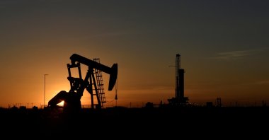 A pump jack operates in front of a drilling rig at sunset in an oil field in Midland, Texas U.S. August 22, 2018. (Reuters Photo)