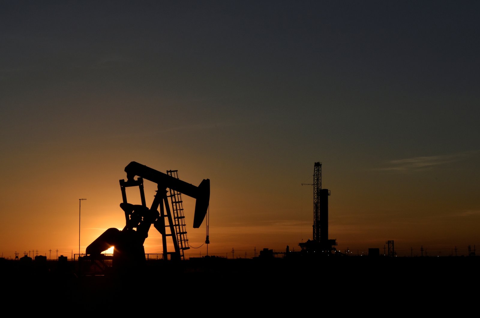 A pump jack operates in front of a drilling rig at sunset in an oil field in Midland, Texas U.S. August 22, 2018. (Reuters Photo)