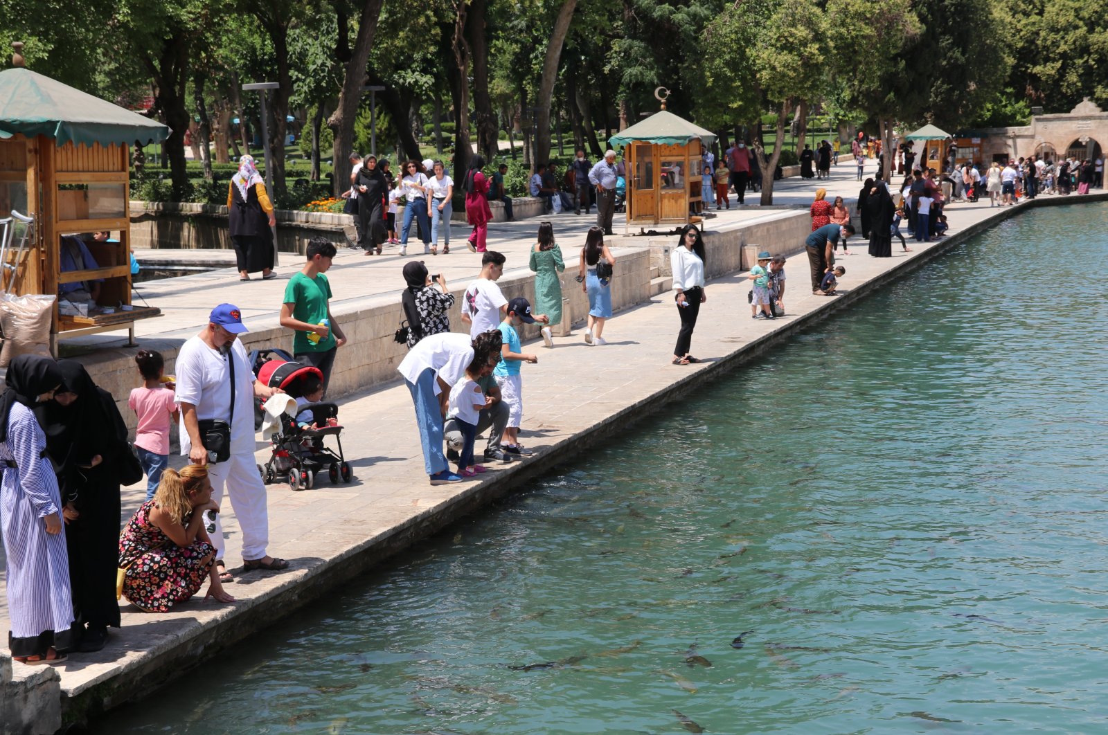 People walk on the shore of Balıklıgöl pond in Şanlıurfa, southeastern Turkey, July 2, 2021. Şanlıurfa has the highest total fertility rate in the country. (AA PHOTO) 