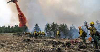 Wildland firefighters watch and take video with their cellphones as a plane drops fire retardant on Harlow Ridge above the Lick Creek Fire, southwest of Asotin, Washington, U.S., July 12, 2021. (Lewiston Tribune via AP)