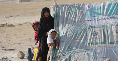An internally displaced Afghan woman stands with her daughters in front a makeshift tent in a camp on a rocky patch of land, after fleeing fighting between the Taliban and Afghan security personnel, on the edge of the city of Mazar-e-Sharif, northern Afghanistan, July 8, 2021. (AP Photo)