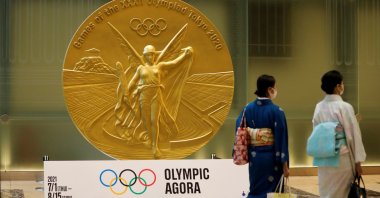 Women wearing protective masks against COVID-19, walk past a large-scale reproduction of the Tokyo 2020 Olympic Games medal at Nihonbashi Mitsui Tower in Tokyo, Japan, July 14, 2021.    (Reuters Photo)
