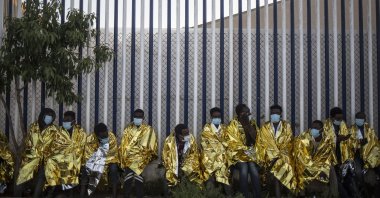 A group of migrants sits wrapped in thermal blankets at a holding center for migrants in the Spanish North African enclave of Melilla, Spain, May 18, 2021. (AP Photo)