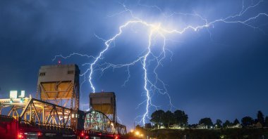 A bolt of lighting strikes over Lewiston, Idaho, behind the Interstate Bridge that spans the Snake River into Clarkston, Washington, U.S., July 1, 2021. (Lewiston Tribune via AP)