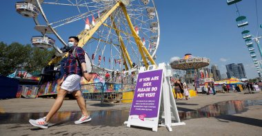 A man wearing a face mask walks by a health safety sign as the Calgary Stampede gets underway following a year off due to COVID-19 restrictions, Alberta, Canada, July 9, 2021. (Reuters Photo)