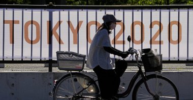 A woman rides her bike past signage for the 2020 Summer Olympics, Tokyo, Japan, July 18, 2021. (AP Photo)