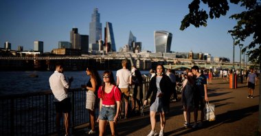 People enjoy the evening sunshine on Thames Embankment by the river Thames with the skyline of the City of London in the background, London, U.K., July 16, 2021. (AFP Photo)