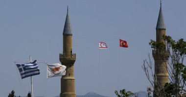 A Turkish and Turkish Republic of Northern Cyprus (TRNC) flags fly on a minaret of the Selimiye mosque, or Cathedral of St Sophia (Agia Sofia) behind Greek (L) and Greek Cypriot flags (2nd L) in divided capital Nicosia, Cyprus, Monday, April 26, 2021. (AP Photo/Petros Karadjias)