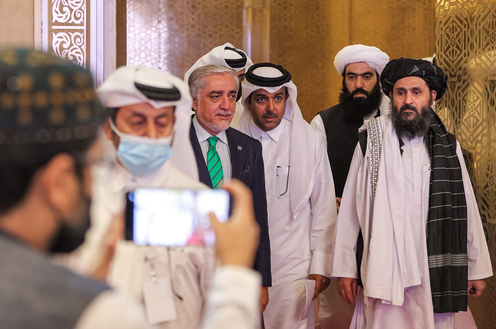 A man uses his phone to take a picture of (L to R) the head of Afghanistan's High Council for National Reconciliation Abdullah Abdullah, Qatar's envoy on counter-terrorism Mutlaq al-Qahtani, and the leader of the Taliban negotiating team Mullah Abdul Ghani Baradar as they arrive to present the final declaration of the peace talks between the Afghan government and the Taliban in Qatar's capital Doha on July 18, 2021. (AFP File Photo)