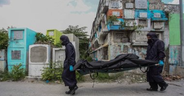 Workers wearing masks, gloves and protective coats carry a body bag containing the skeletal remains of Rodzon Enriquez, who was killed five years ago in the country's war on drugs, after they were exhumed at a cemetery in Manila, the Philippines, July 8, 2021. (AFP Photo)