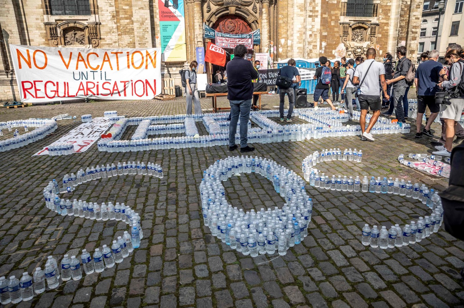 The words "help" and "SOS" are spelled with water bottles during a demonstration in front of the Saint John the Baptist at the Beguinage church, occupied by undocumented immigrants, Brussels, Belgium, July 19, 2021. (AFP Photo)