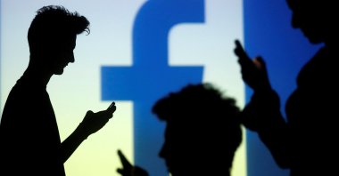 People are silhouetted as they pose with mobile devices in front of a screen projected with a Facebook logo, in this picture illustration taken in Zenica Oct. 29, 2014. (Reuters Photo)