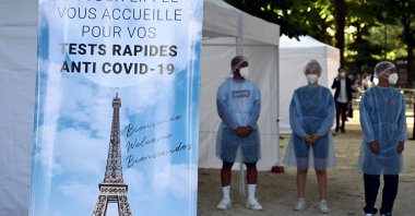 Health workers stand near a COVID-19 test area, as a banner reads 'The Eiffel Tower welcomes you for your anti COVID-19 quick tests', near the Eiffel Tower in Paris, France, on July 21, 2021. (AFP Photo)