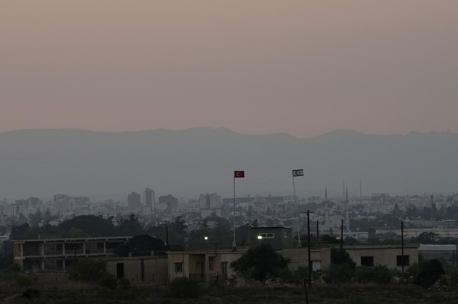A Turkish military guard post with a Turkish flag (L) and Turkish Cypriot flag with Maraş (Varosha) in the background, prior to the Turkish President's visit to Turkish Cyprus, in Dherynia, TRNC, July 19, 2021. (AP Photo)