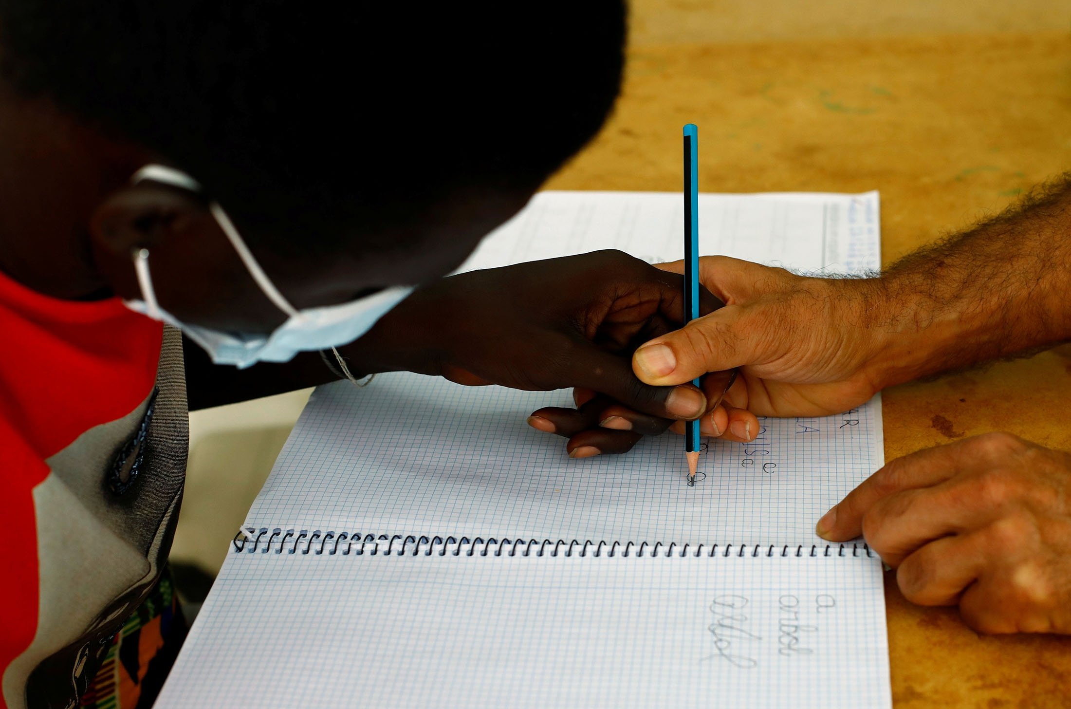 Tito Martin takes the hand of Mor Low (L), a migrant from Senegal, to teach him how to write letters in Spanish, in Las Palmas, on the island of Gran Canaria, Spain, July 21, 2021. (Reuters Photo)